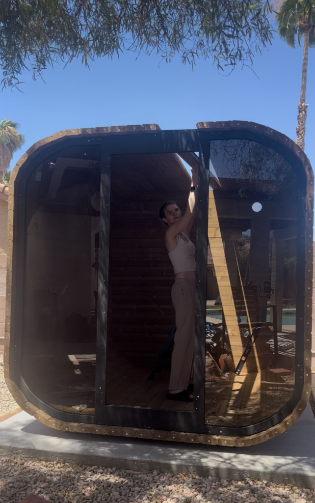 Emily reaching overhead to adjust the upper section of the wooden sauna during assembly.