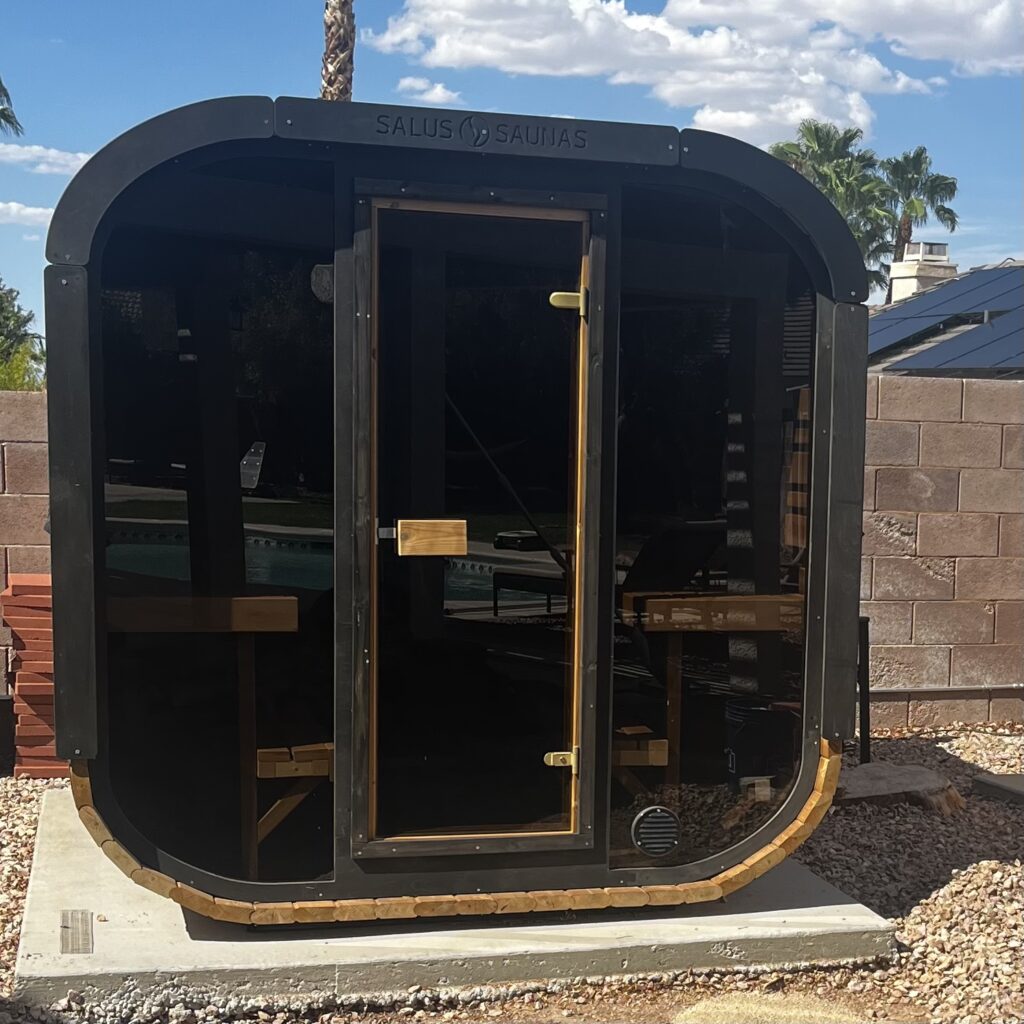 Completed outdoor wooden sauna with a dark curved roof, glass front, and wooden benches inside.