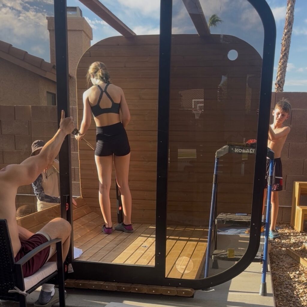 Family members helping hold the sauna's glass front wall upright during assembly.