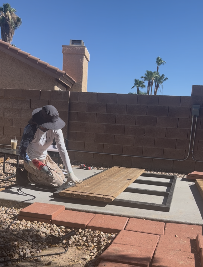 Emily wearing a sun hat and long-sleeved shirt while working on wooden boards laid out in the backyard.