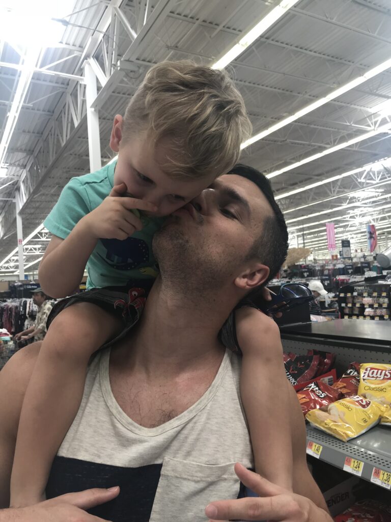 A child leans toward a man while sitting on his shoulders.