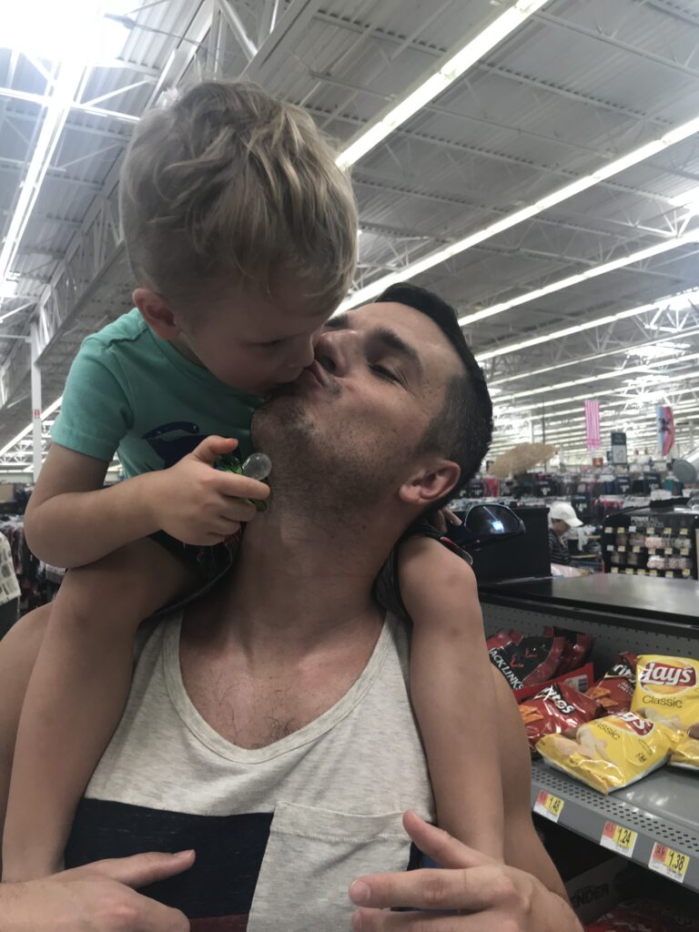 A man kisses a child seated on his shoulders in a store.