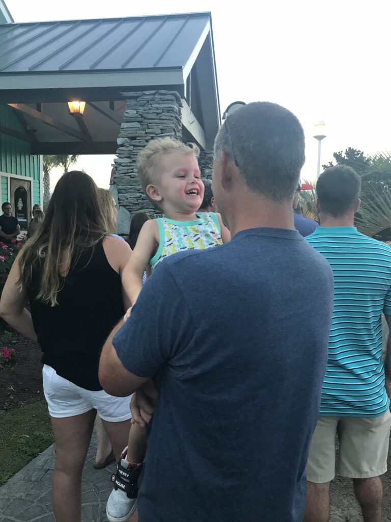 A smiling child is held in a man's arms outdoors.