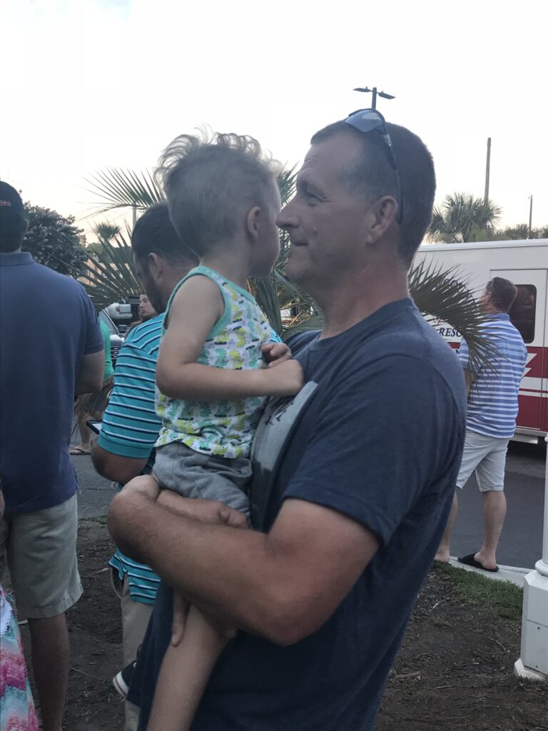 A man holds a child face to face outdoors.