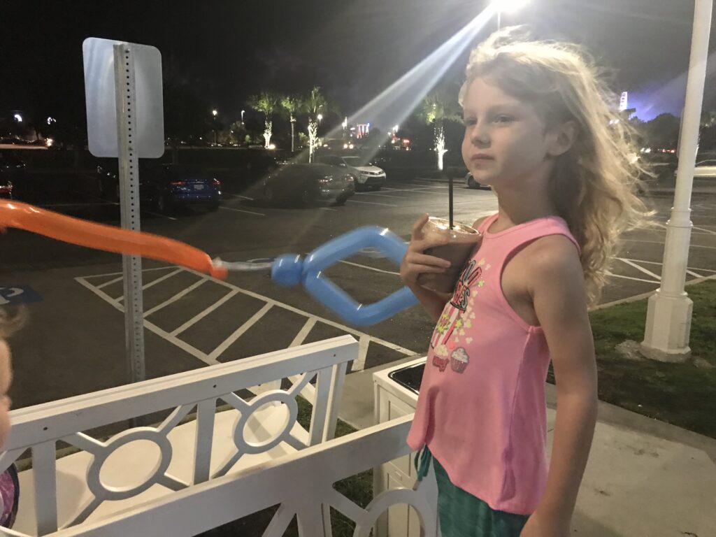 A child holds a colorful balloon creation beside a white railing at night.