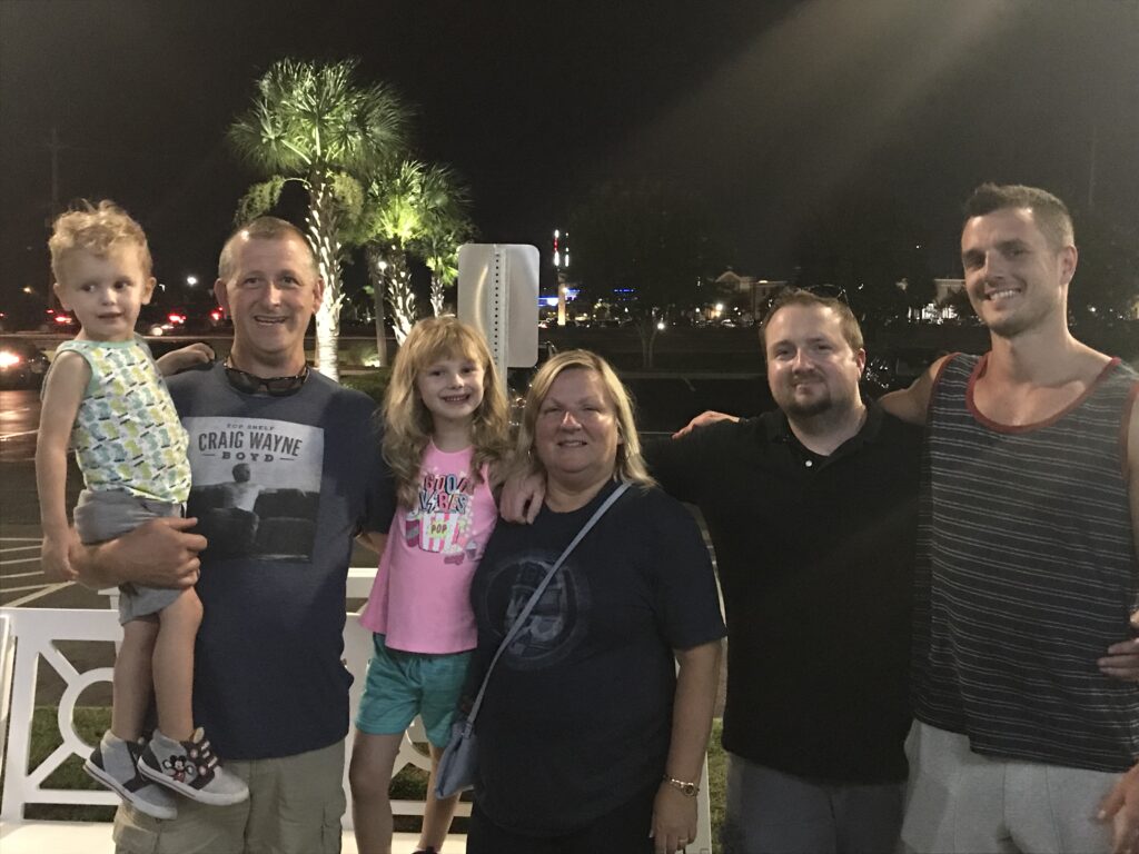 Four adults and two children posing beside a white railing outdoors at night.