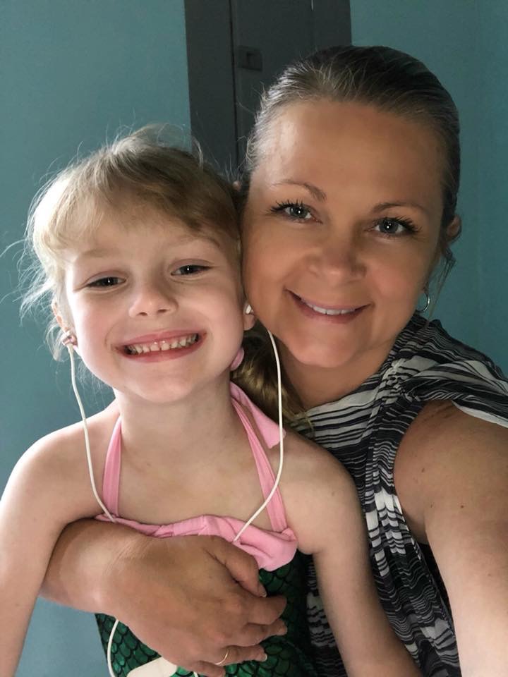 An adult and a child in a pink top smiling together for a close-up indoor photo.