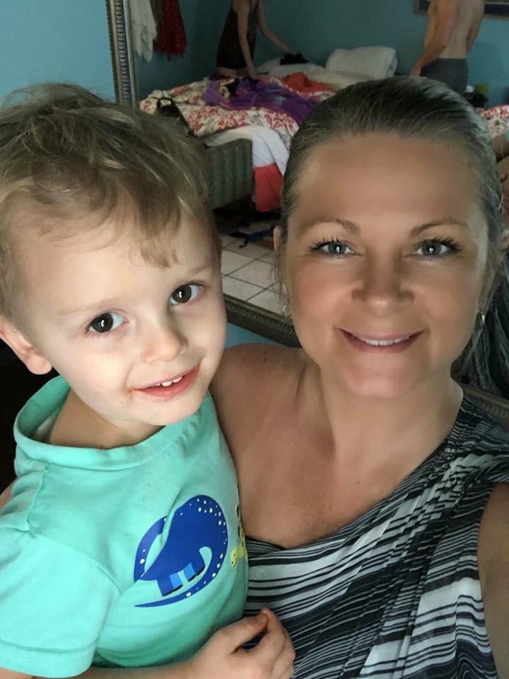 An adult holding a smiling young child in a turquoise shirt indoors.