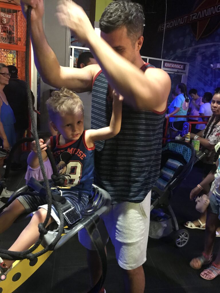 A young child sitting in a yellow suspended chair while an adult holds the ropes above.