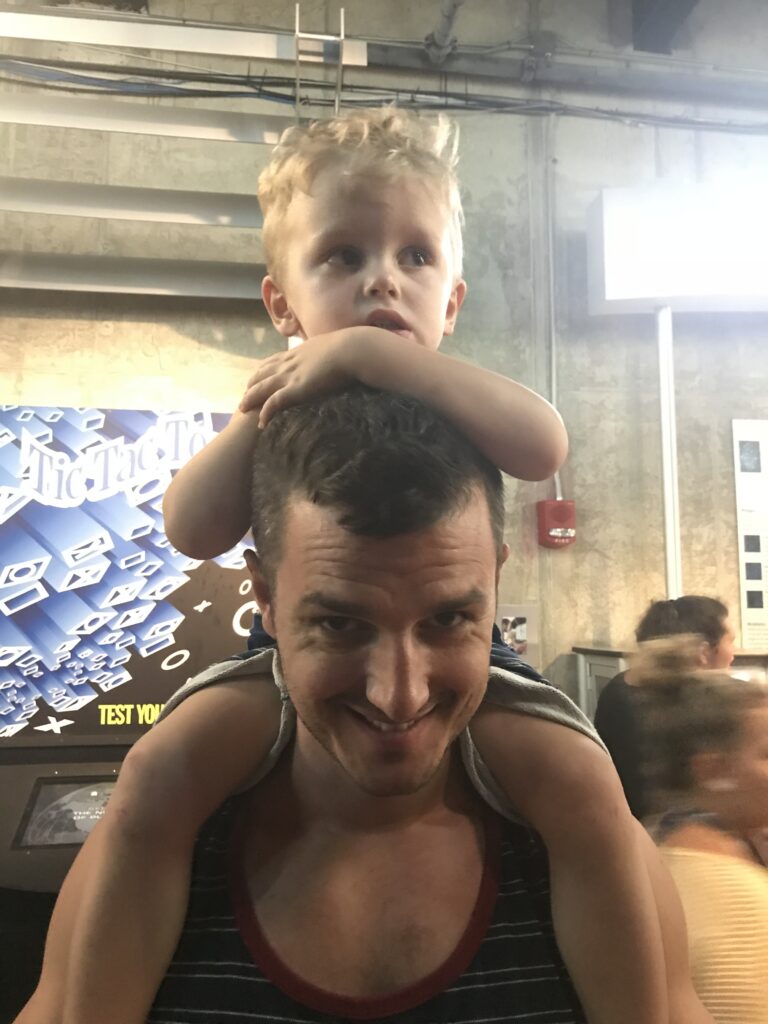 A young child sitting on an adult's shoulders with their arms resting on the adult's head.