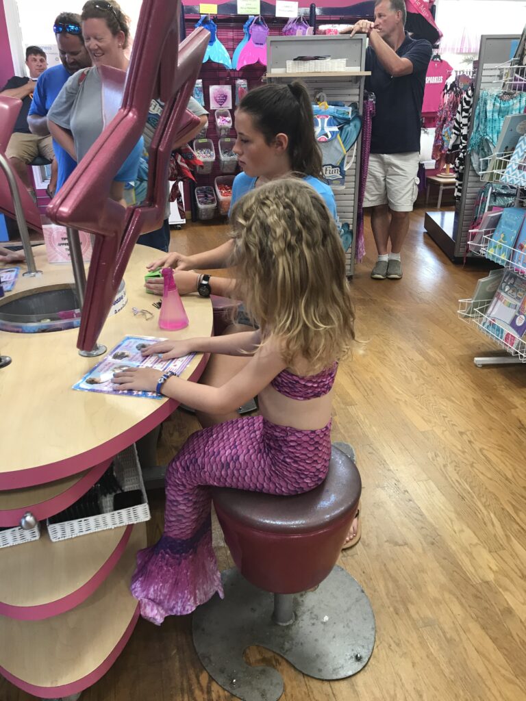 A child in a pink mermaid costume sitting at a counter with star-shaped mirrors.