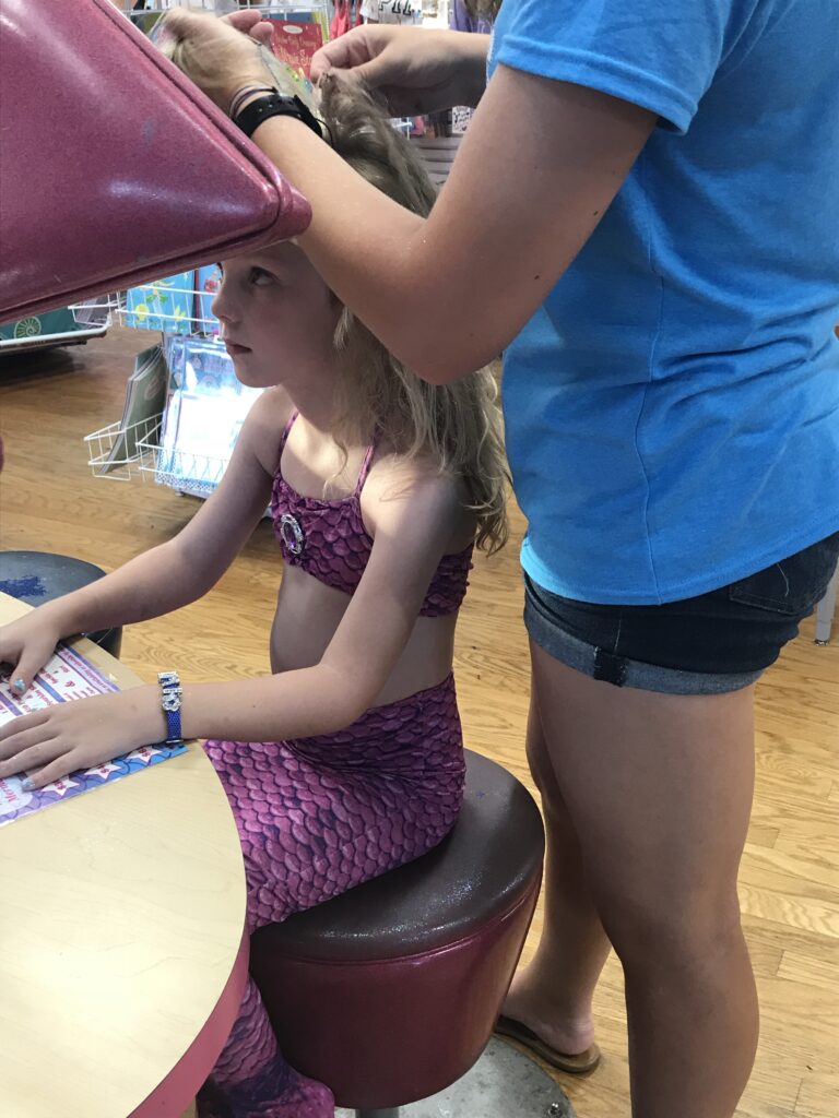 A child in a pink mermaid costume having their hair styled while seated at a counter.
