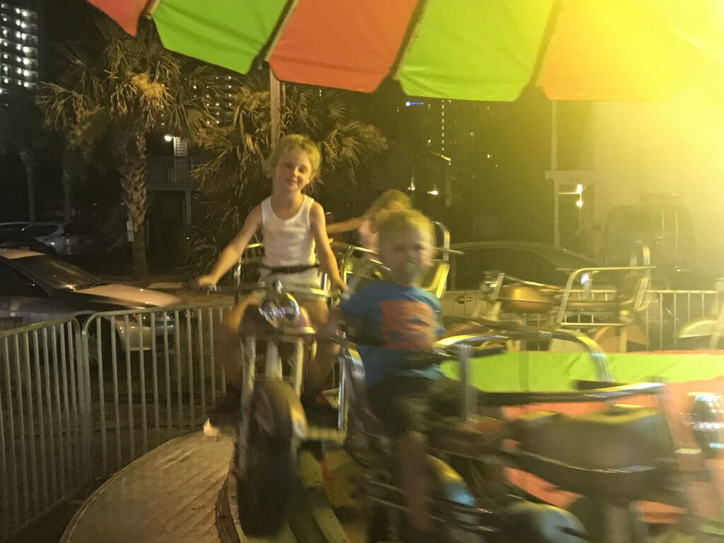 Children ride a carousel beneath a brightly colored canopy.