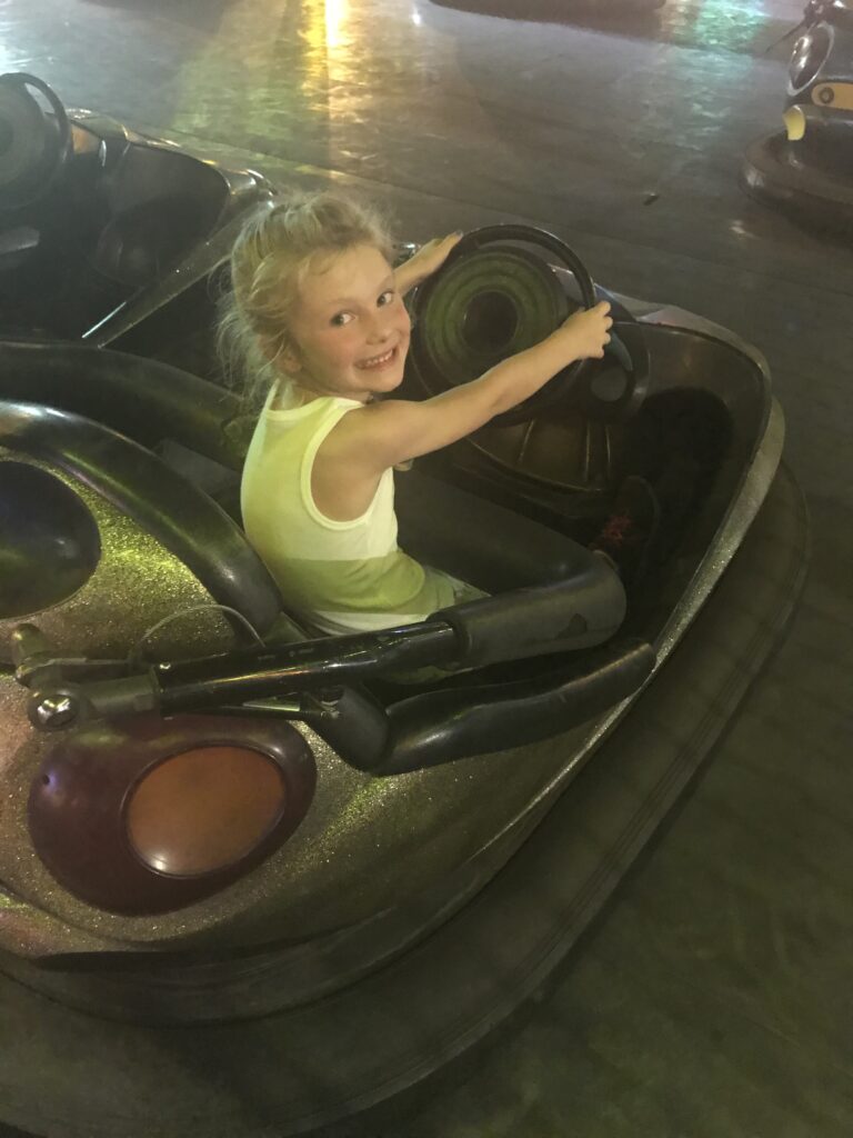 A smiling child holds the steering wheel of a bumper car.