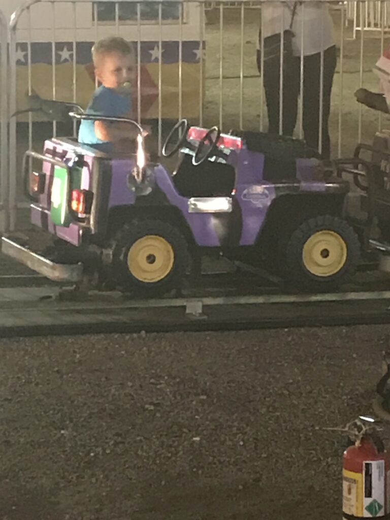 A child sits behind the wheel of a purple jeep-shaped amusement ride.